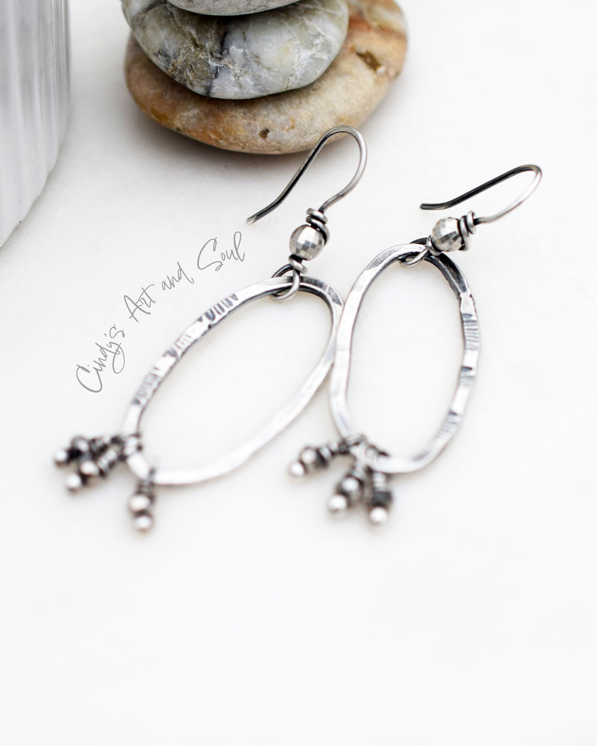 all silver hoop earrings hanging from a white bowl with a stack of stones next to it.