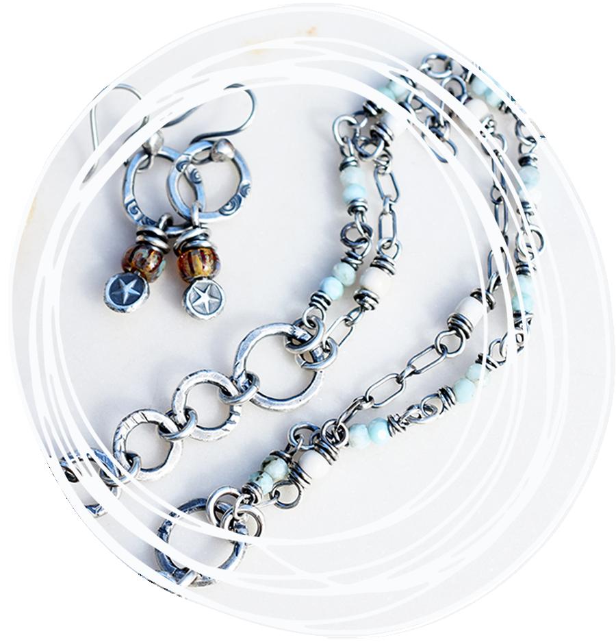 Silver bracelet with a bar engraved 'beach girl' and a starfish symbol, featuring a blue bead, displayed on a light-colored surface with a white swirl border.