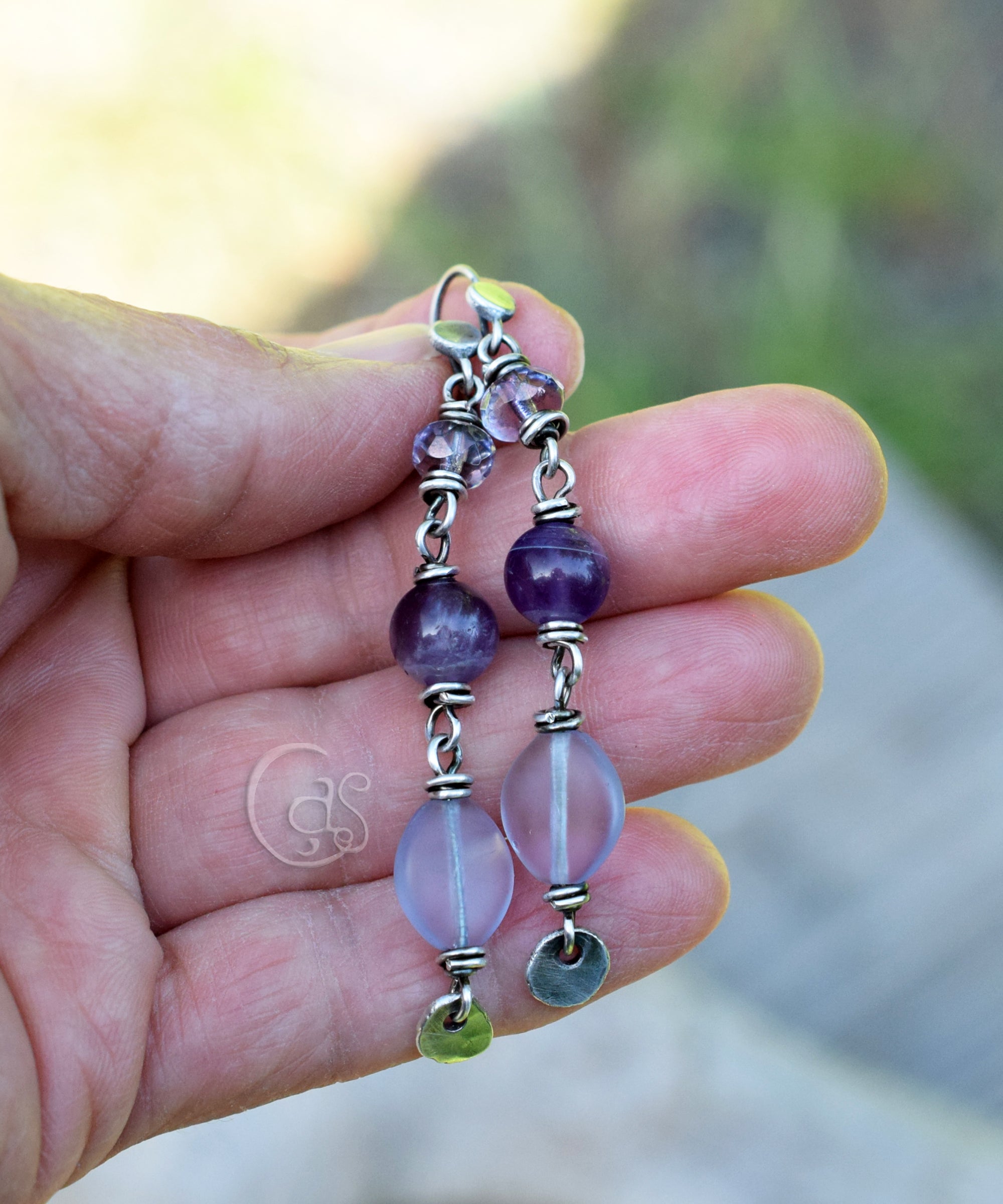 Hand holding a pair of beaded earrings with purple and pink beads.