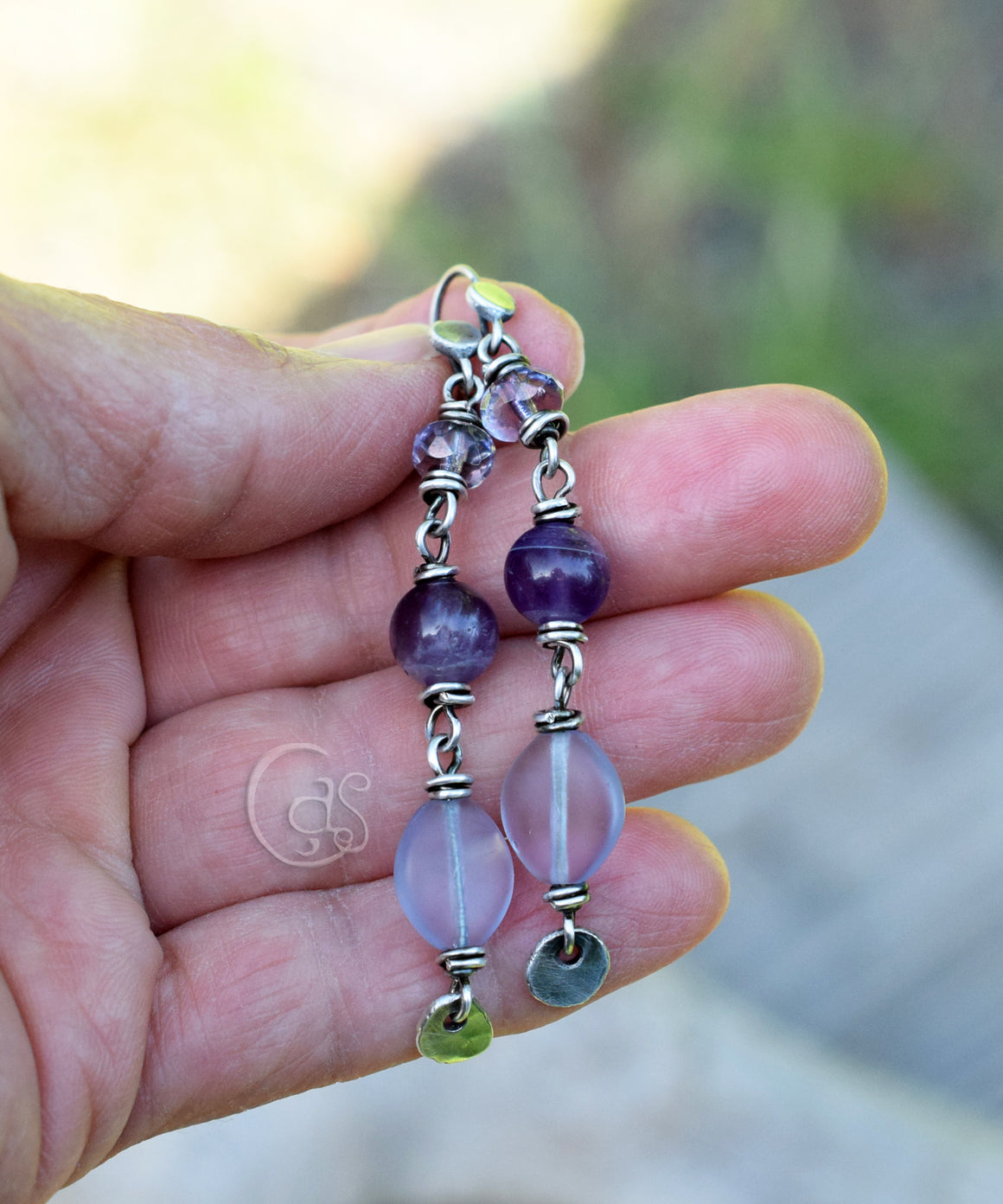 Hand holding a pair of beaded earrings with purple and pink beads.