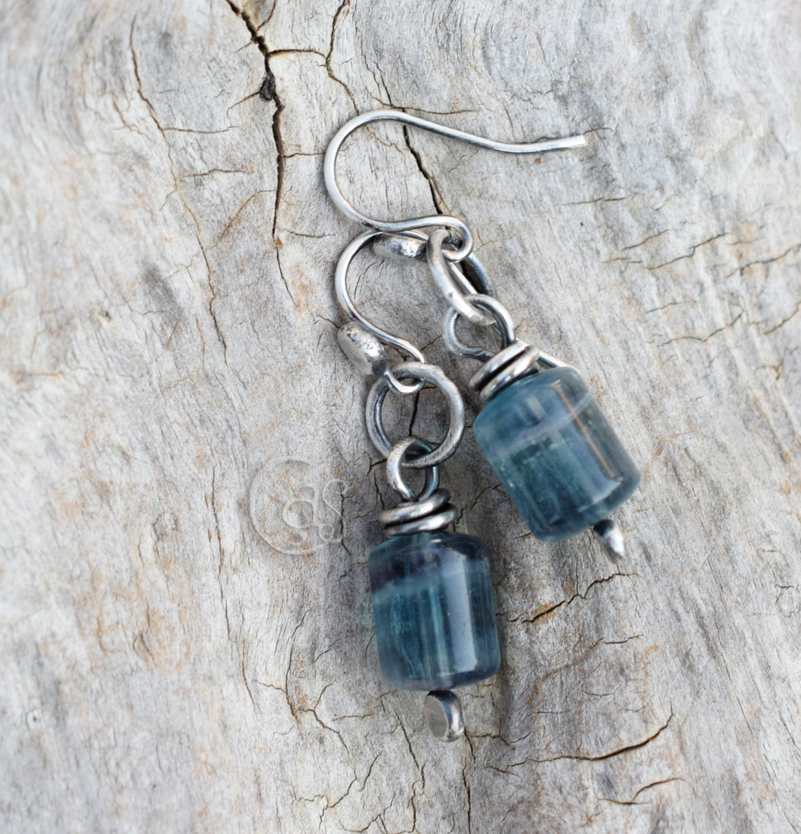 Silver earrings with blue beads on a textured stone surface