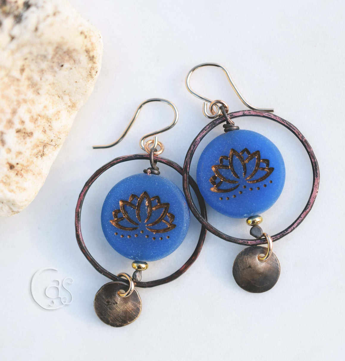 bronze hoop earrings on a white background next to a rock
