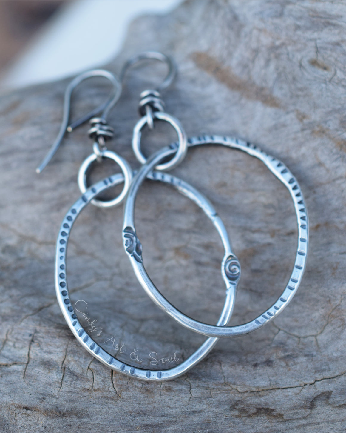 Handmade sterling silver hoop earrings with textured edges and fishhook wires, displayed on a rustic piece of wood.