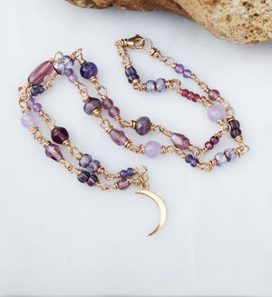 crescent moon necklace with golden bronze metal. Beaded chain with beads in various shades of purple. 