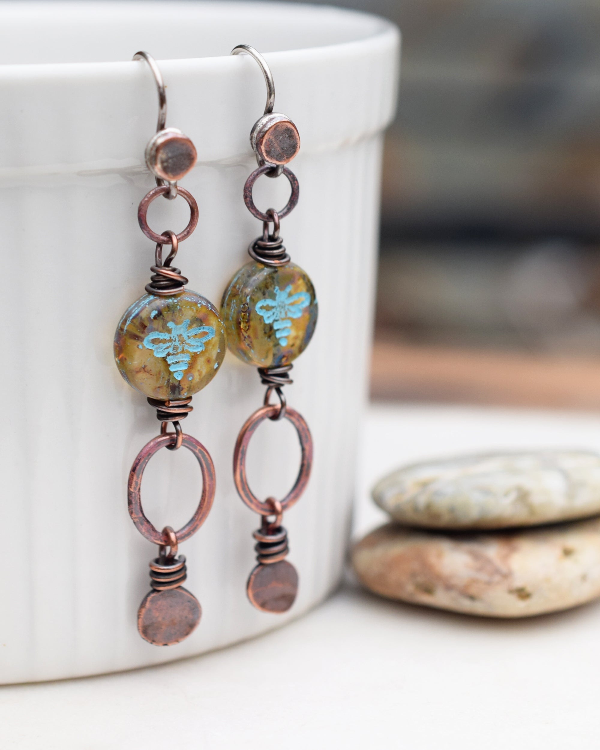 A pair of earrings with blue and amber beads, wrapped in copper wire with hammered copper nugget charms and hoops dangling below.