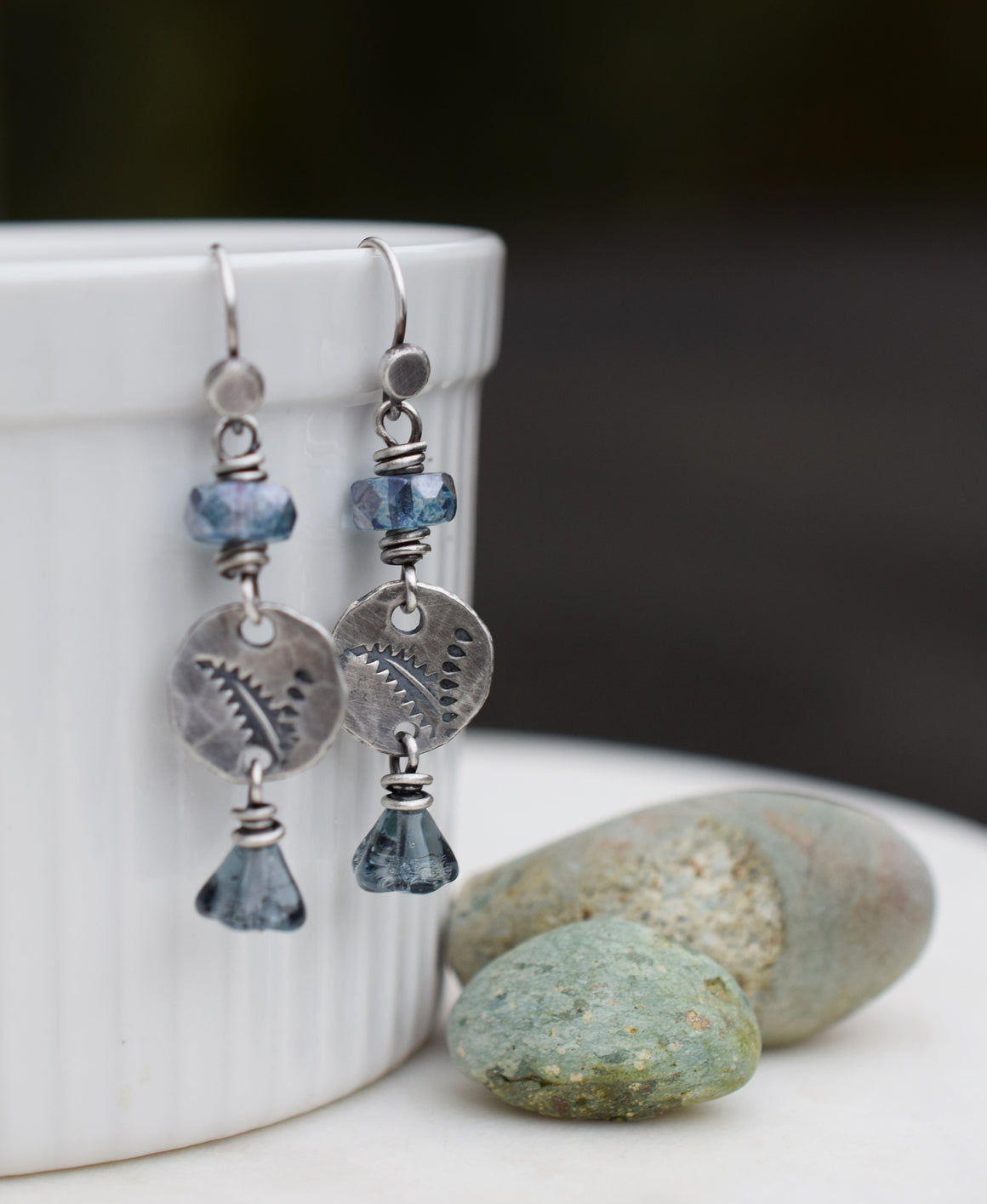Pair of earrings with blue beads and silver accents on a white surface with pebbles.