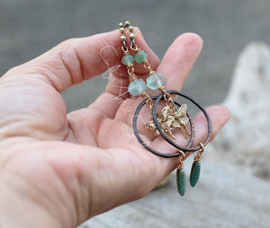 Hand holding a delicate necklace with green beads and gold accents against a blurred background