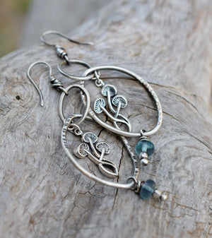 Silver earrings with mushroom designs and blue beads on a wooden surface