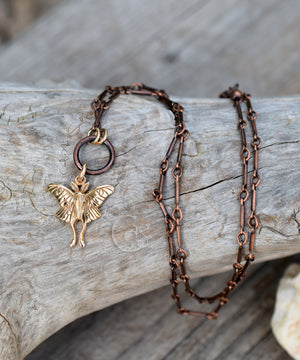 Copper chain necklace with a fairy pendant on a wooden surface