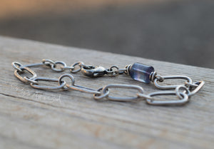Silver chain bracelet with a blue bead on a wooden surface