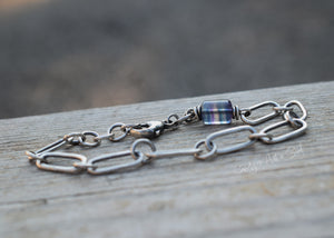 Silver chain bracelet with a blue glass bead on a wooden surface