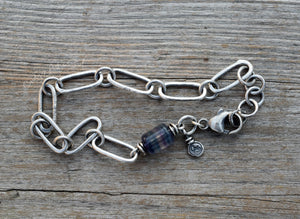 Silver chain bracelet with a blue beaded charm on a wooden surface