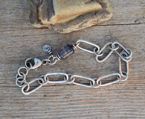 Silver chain bracelet with a purple bead on a wooden surface