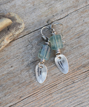 Pair of earrings with green beads and silver charms on a wooden surface