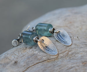 Pair of earrings with green beads and silver components on a wooden surface