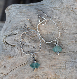 Silver hoop earrings with green gemstones on a wooden surface