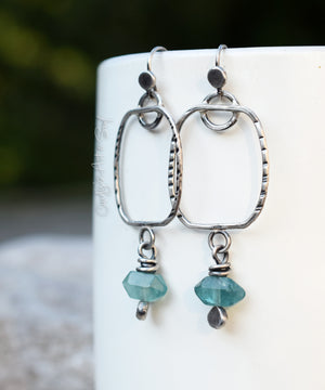 Silver hoop earrings with teal beads on a white surface
