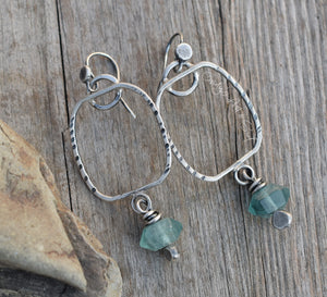 Silver hoop earrings with green beads on a wooden surface