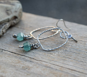 Silver earrings with green beads on a wooden surface
