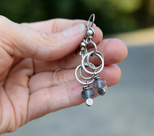 Hand holding a silver earring with beads against a blurred background