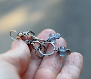 Silver jewelry piece held between fingers with a blurred background
