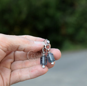 Hand holding a pair of earrings with clear stones against a blurred natural background