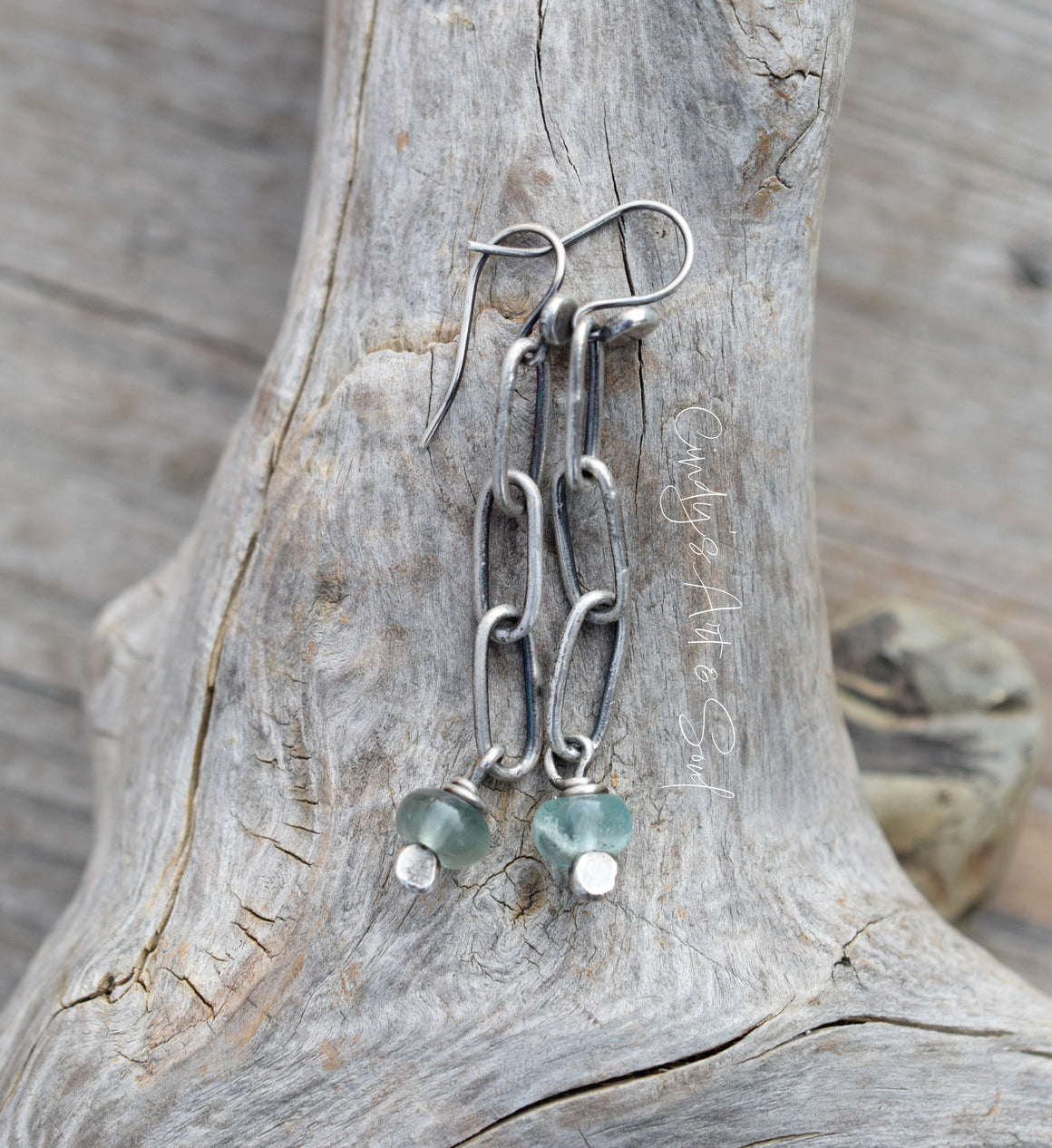 Silver chain earrings with green gemstones on a wooden surface