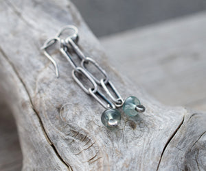 Silver earrings with green gemstones on a wooden surface