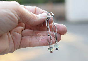 Hand holding a pair of silver chain earrings with beads against a blurred background