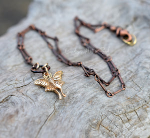 Copper necklace with a butterfly pendant on a textured stone surface