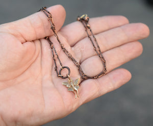 Hand holding two necklaces with fairy pendants against a blurred background