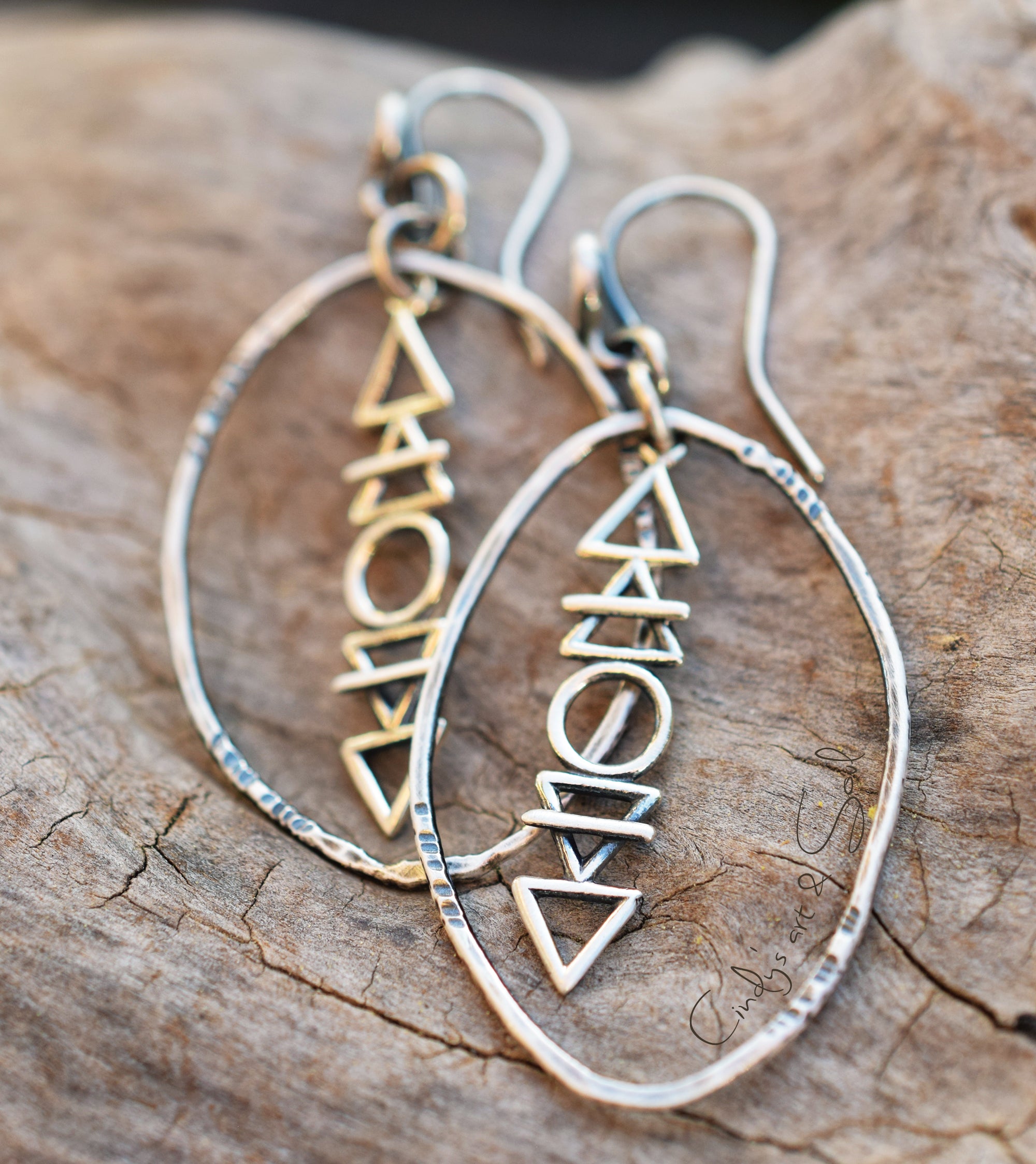 Pair of silver hoop earrings with geometric triangle designs on a wooden surface