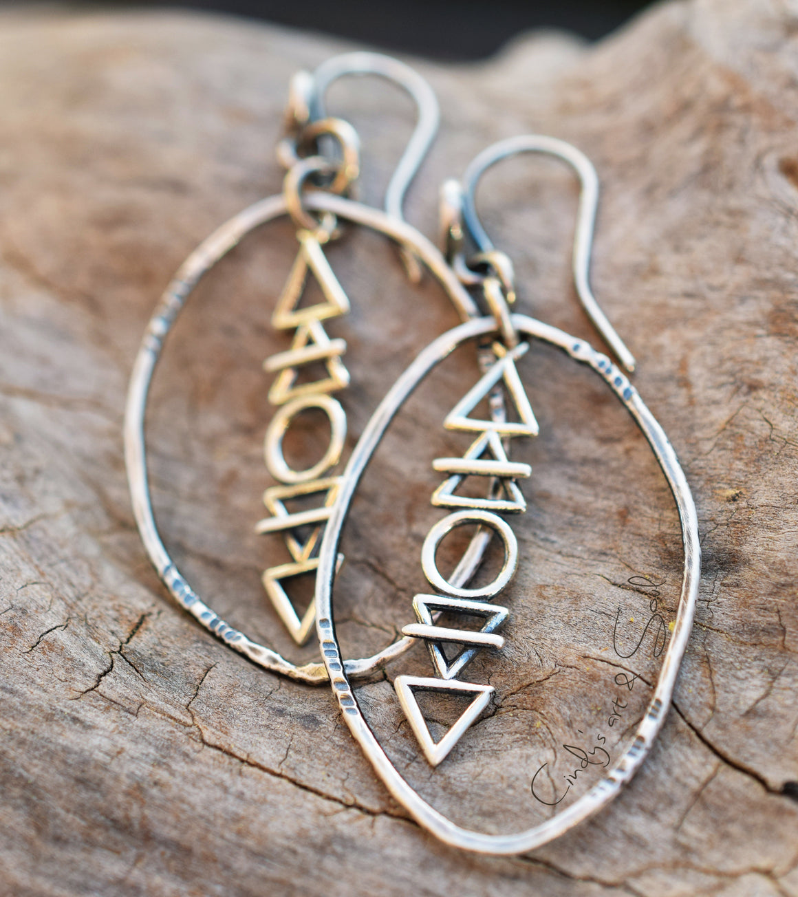 Pair of silver hoop earrings with geometric triangle designs on a wooden surface