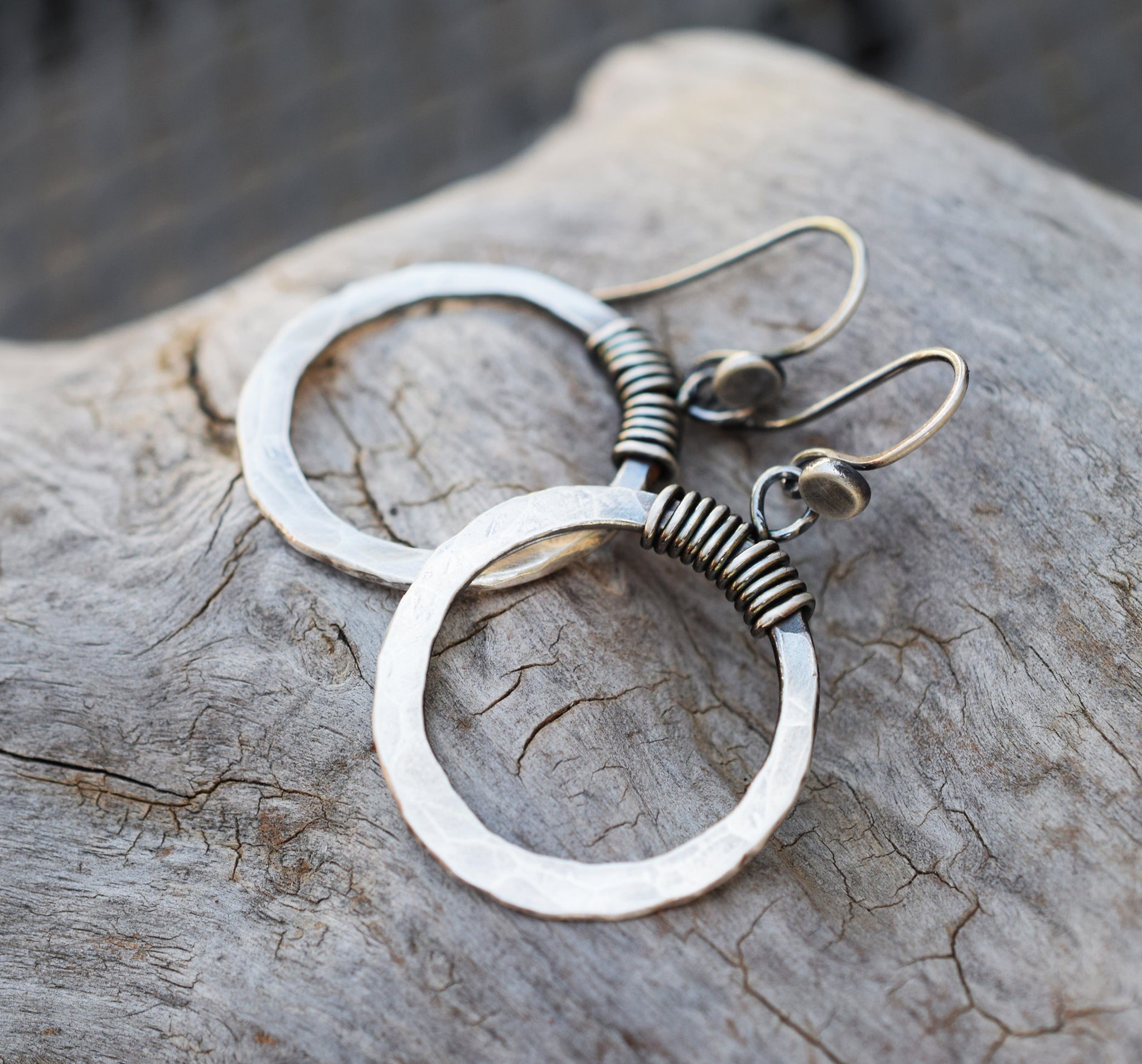 A pair of silver hoop earrings with wrapped silver wires, displayed on a textured wooden surface.