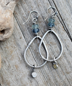 Silver hoop earrings with blue beads on a wooden surface