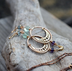 Gold hoop earrings with gemstones on a stone surface