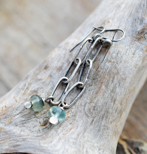 Silver earrings with green gemstones on a wooden surface