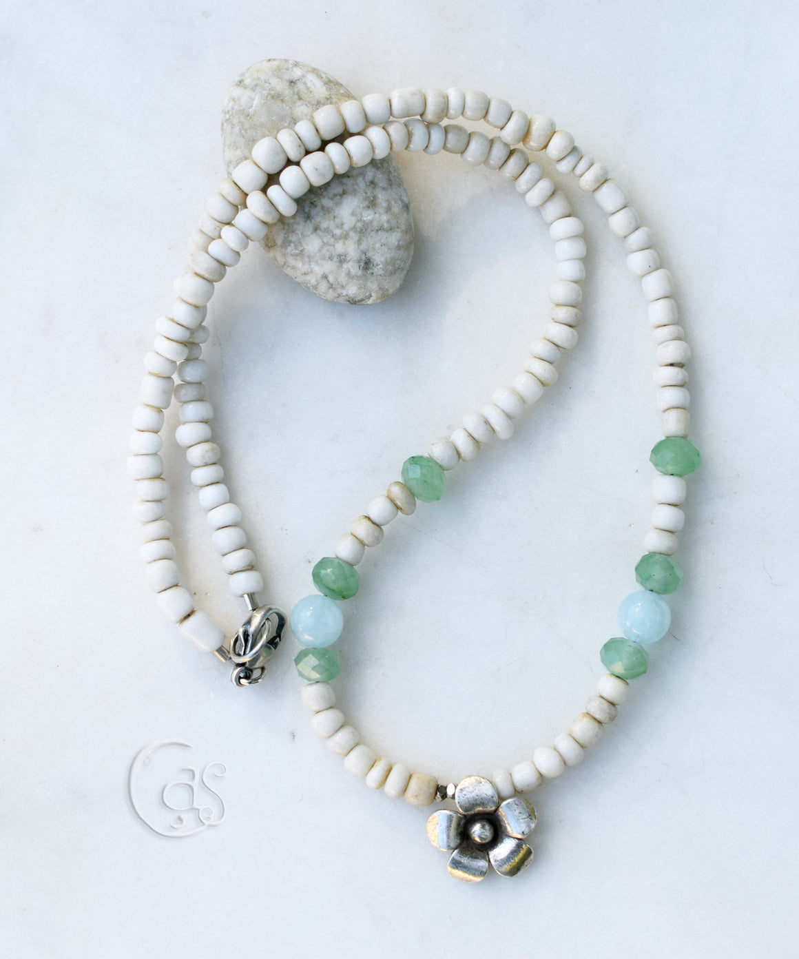 beaded necklace with white blue and green beads and a silver flower at the center on a white background.
