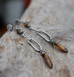 Long Silver earrings with brown beads on a wood background.
