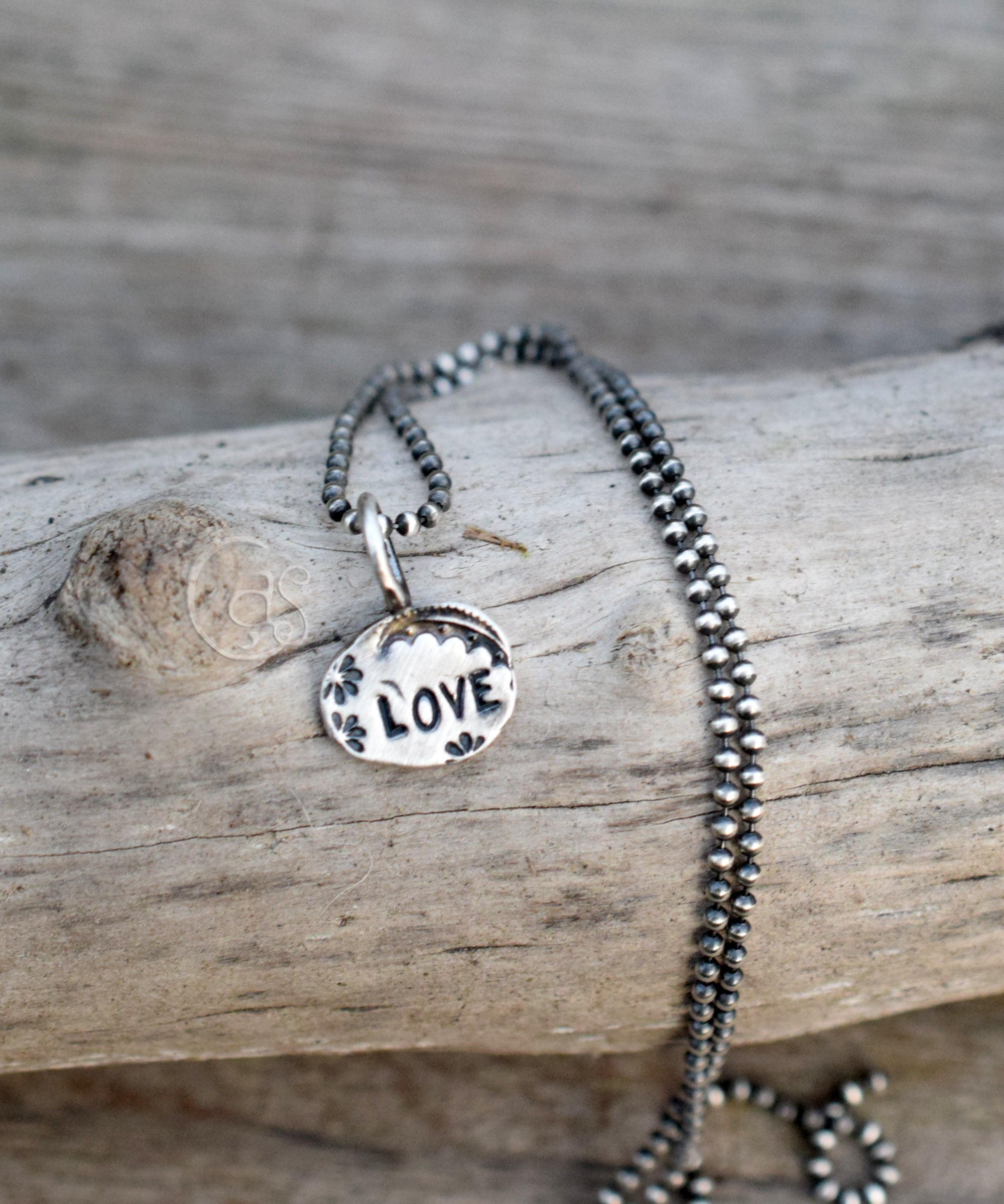 silver pendant with the word love on a wood background.