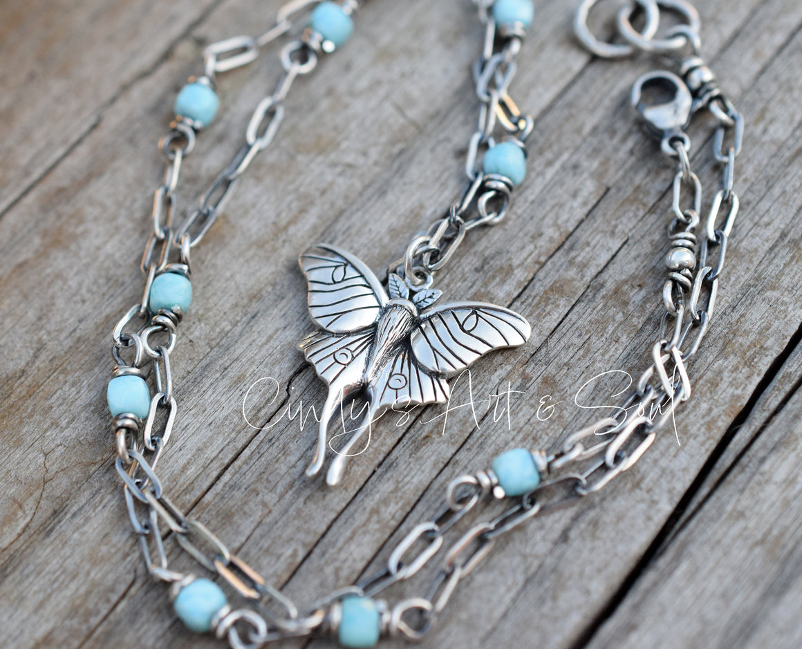Necklace with luna moth charm and turquoise beads on a wooden surface