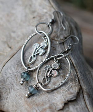 Silver earrings with leaf designs and blue beads on a wooden surface
