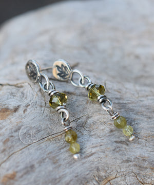 Silver post earrings with sparkling green beads on a wood background. 
