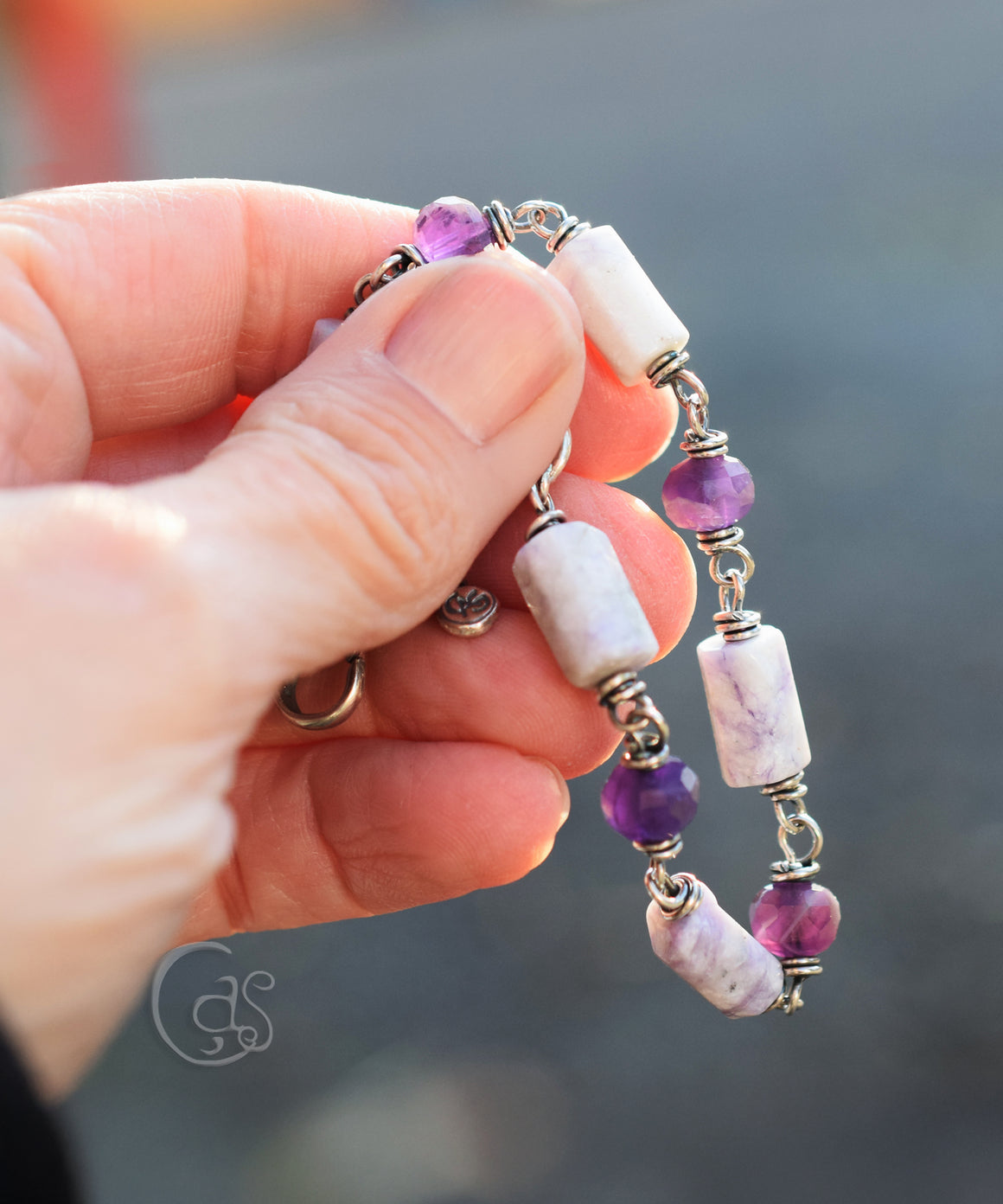 a hand holding a purple and mixed white and purple stone bracelet. 