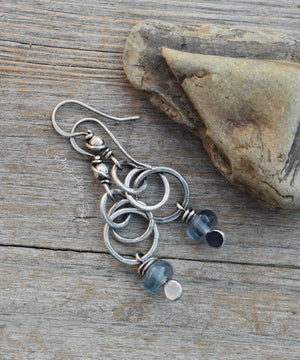 Silver earrings with blue beads on a wooden surface with a stone.