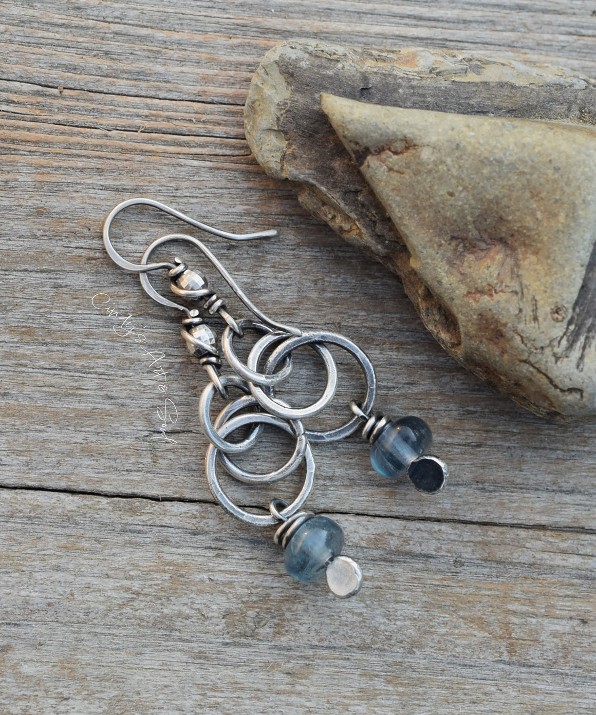Silver earrings with blue beads on a wooden surface with a stone.
