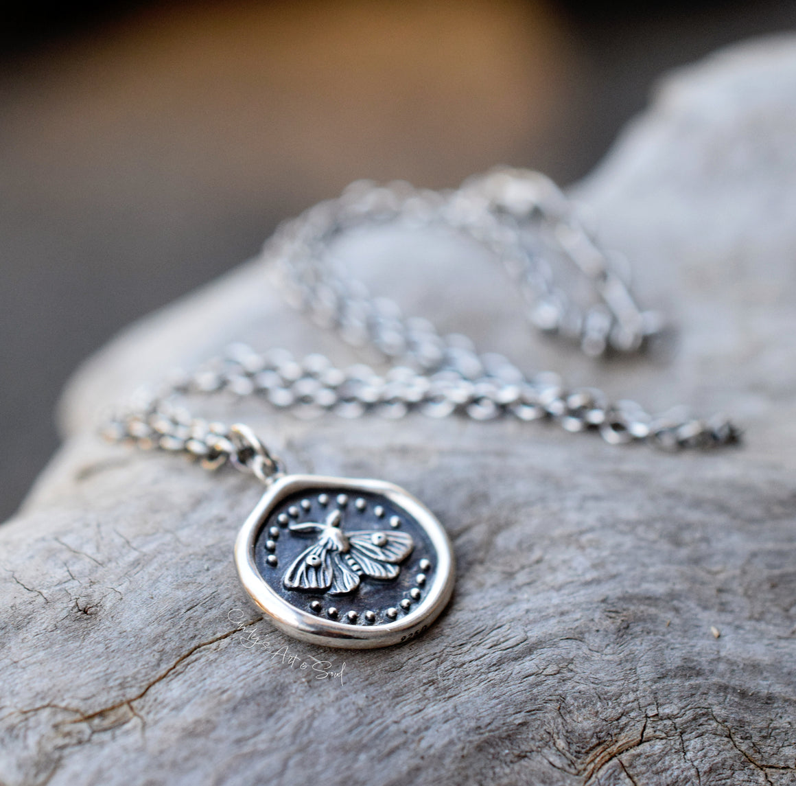 Silver necklace with a moth pendant on a wood surface.