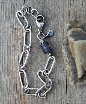 Silver chain bracelet with a blue beaded charm on a wooden surface