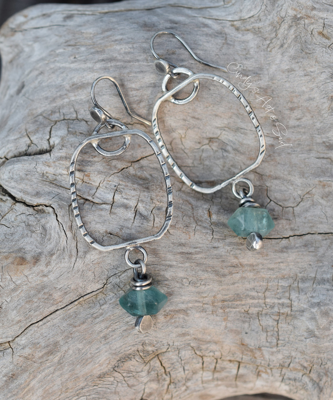 Silver earrings with green gemstones on a wooden surface