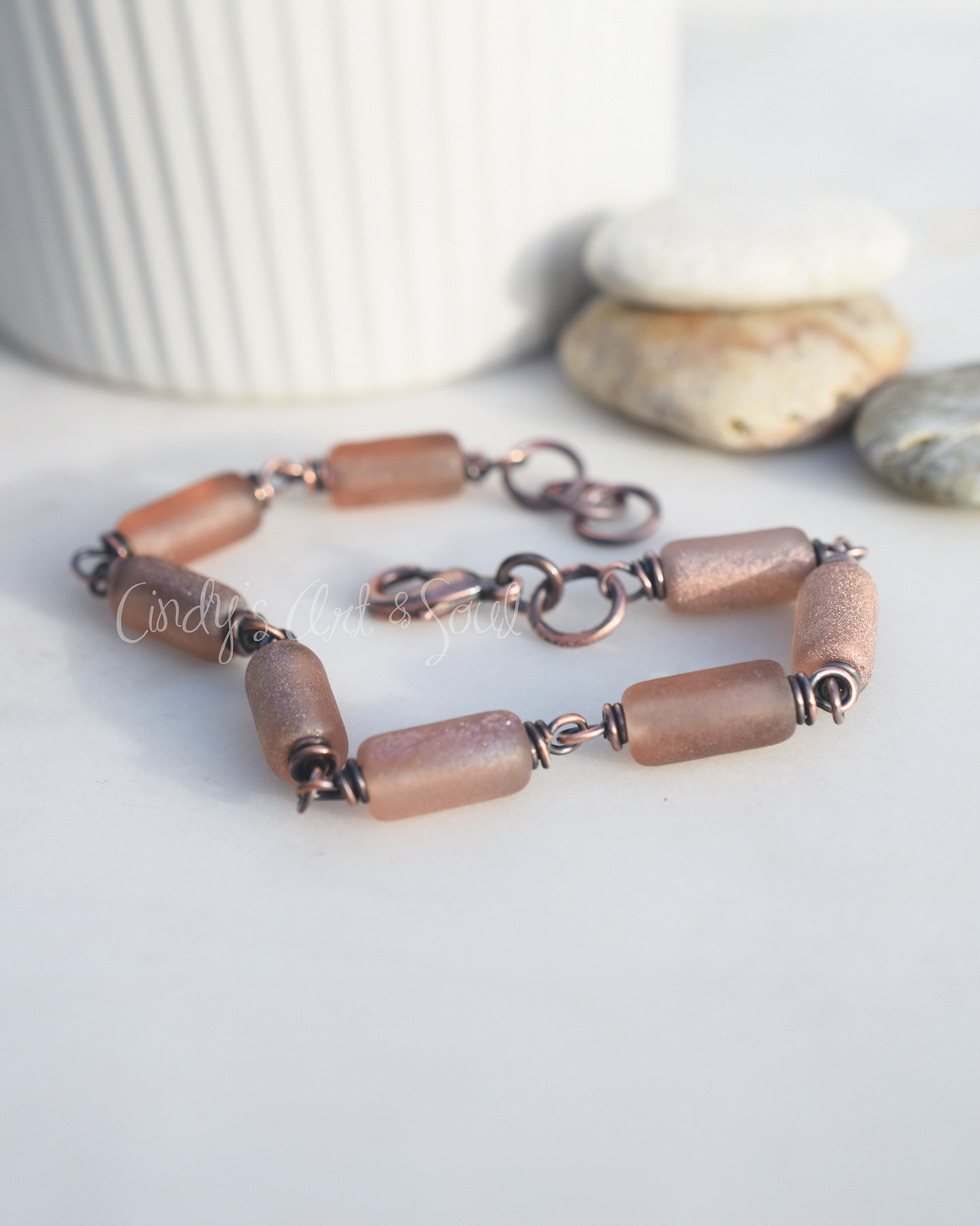 A handcrafted bracelet with golden blush-colored Czech glass beads, wrapped in copper wire, featuring a copper lobster clasp and a small length of fused copper chain.